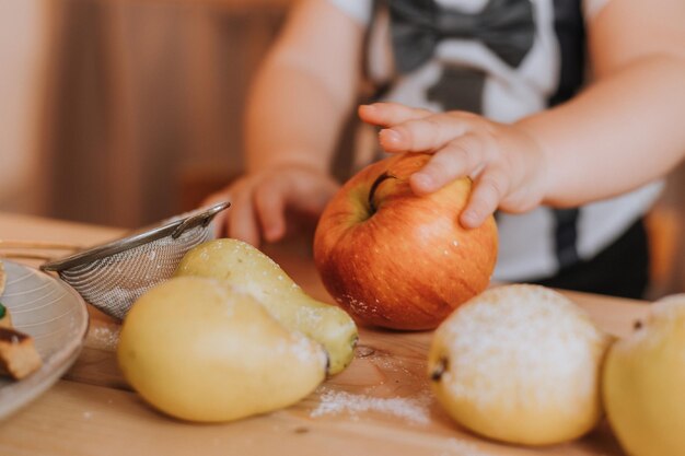 Nahaufnahme der Hände des Babys, die einen Apfel halten. kleiner Junge in einem T-Shirt mit der Nummer eins. ersten Geburtstag in festlicher Atmosphäre. Foto in hoher Qualität