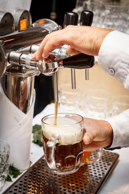 Nahaufnahme der Hände des Barkeepers am Zapfhahn, der ein gezapftes Craft-Bier in einen Glaskrug gießt