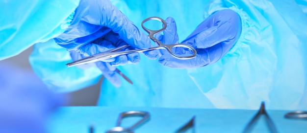 Nahaufnahme der Hände des Chirurgen bei der Arbeit im Operationssaal, blau getönt