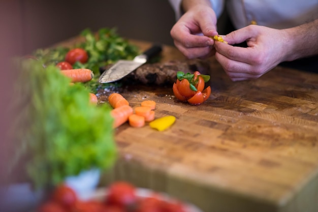 Nahaufnahme der Hände des Küchenchefs in der Hotel- oder Restaurantküche, die Rindersteak mit Gemüsedekoration zubereitet?