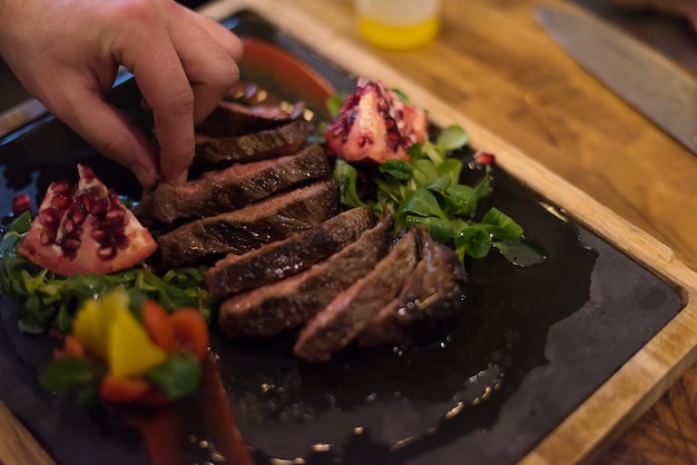 Nahaufnahme der Hände des Küchenchefs in der Hotel- oder Restaurantküche, die Rindersteak mit Gemüsedekoration zubereitet?