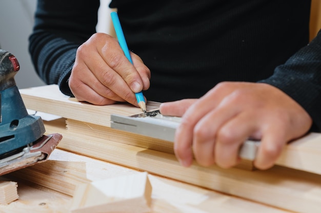 Nahaufnahme der Hände des Zimmermanns, die das Brett vor Arbeitsbeginn mit einem Bleistift markieren Herstellung von Holzprodukten Professioneller Meister