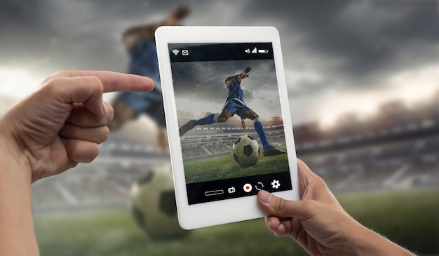 Nahaufnahme der Hände, die Tablet-Anzeigen von Sport, Fußball-Online-Streaming der Meisterschaft halten. Neue Regeln während des Ausbruchs des Coronavirus und der Sperrung von Ländern. Konzept des Sports, des Wettbewerbs, der Technologien.