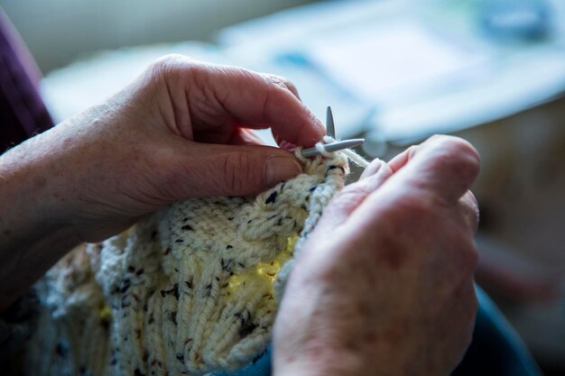 Nahaufnahme der Hände einer älteren Frau, die einen Pullover stricken