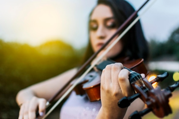 Nahaufnahme der Hände einer Frau, die draußen Geige spielt Ein Mädchen mit ihrer Geige, die draußen eine Melodie spielt Gesicht einer Frau, die Geige spielt Porträt eines Mädchens, das Geige spielt