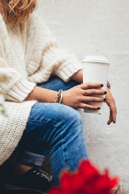 Nahaufnahme der Hände einer Frau vor dem Öffnen des Deckels ihrer weißen Einwegtasse mit Kaffee