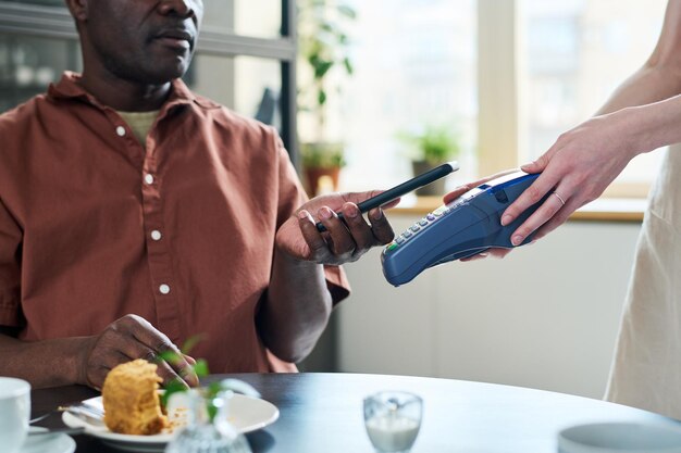 Nahaufnahme der Hände einer Kellnerin, die ein Zahlungsterminal vor dem Verbraucher hält