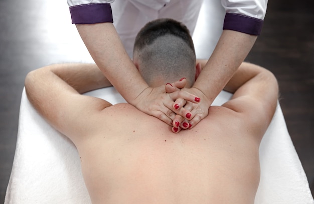 Nahaufnahme der Hände einer Massagetherapeutin beim Kneten und Massieren des männlichen Rückens.