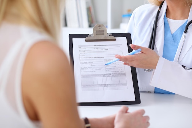 Foto nahaufnahme der hände eines arztes und eines patienten, während der arzt in der zwischenablage auf das anamneseformular zeigt. medizin- und gesundheitskonzept