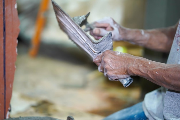 Nahaufnahme der Hände eines Bauarbeiters, der eine Mörtelpfanne zum Verputzen von Wänden mit Zement auf der Baustelle hält