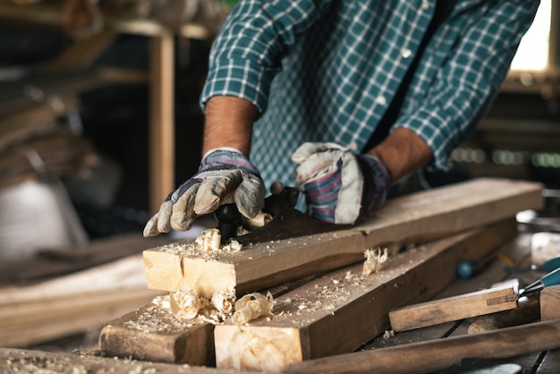 Nahaufnahme der Hände eines behandschuhten Zimmermanns mit einem Handhobel behandelt Holz