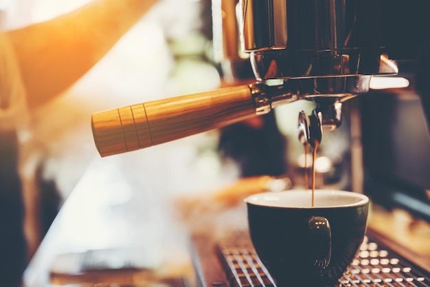 Nahaufnahme der Hände eines jungen männlichen Barista, der Milch gießt und Latte-Kunst in einem frisch gebrühten Kaffee in der Cafeteria-Theke für Kunden herstellt