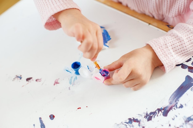 Nahaufnahme der Hände eines Kindes, die mit bunten Pinseln und Farben malen