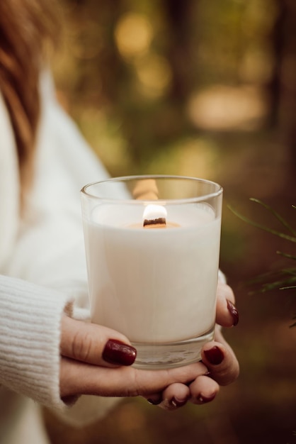 Nahaufnahme der Hände eines Mädchens, das eine brennende Kerze im Freien im Herbstwald hält Konzept der warmen Natur, die eine schöne Zeit in der Natur hat