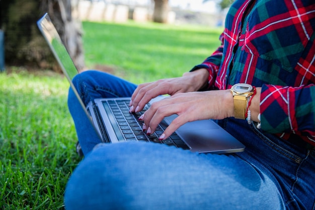 Nahaufnahme der Hände eines Mädchens, die auf ihrem Laptop in einem öffentlichen Park sitzen