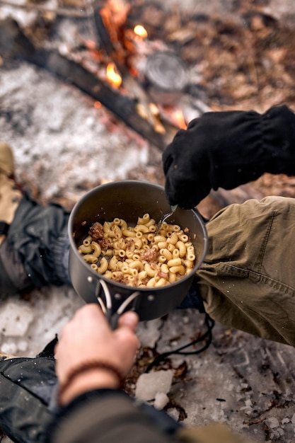 Nahaufnahme der Hände eines Mannes, der allein am Lagerfeuer sitzt und schöne Ferien im Freien verbringt. Reisender, der selbstgemachtes Essen im Wald isst