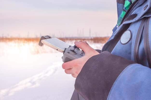 Nahaufnahme der Hände eines Mannes, der eine drahtlose Fernbedienung der Drohne mit Telefonwinterzeit im Feld hält.