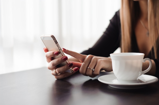 Nahaufnahme der Hände Frau, die ihr Handy im Restaurant, Café verwendet.