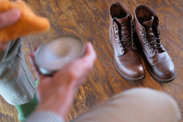 Nahaufnahme der Hände mit Taschentuch und Schuhcreme gegen Paar Lederstiefel, Mann putzt Schuhe