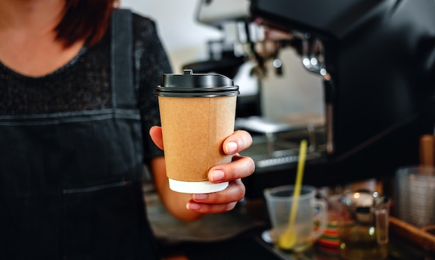 Nahaufnahme der Hand Barista hält in den Händen heißen Kaffee in einem Pappbecher zum Mitnehmen Kaffee zum Mitnehmen