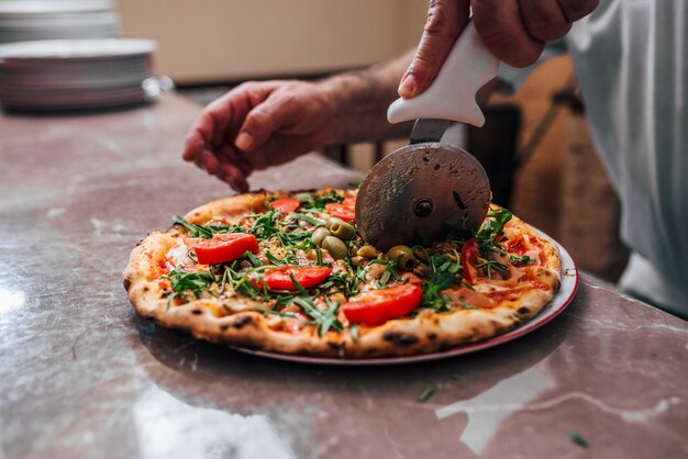 Nahaufnahme der Hand der Chefbäcker-Ausschnittpizza.