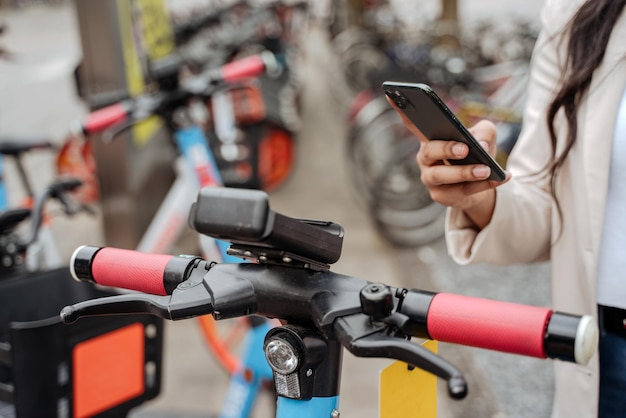 Nahaufnahme der Hand der Frau mit mobiler App, QR-Code scannen, um Elektroroller auf der Straße zu mieten