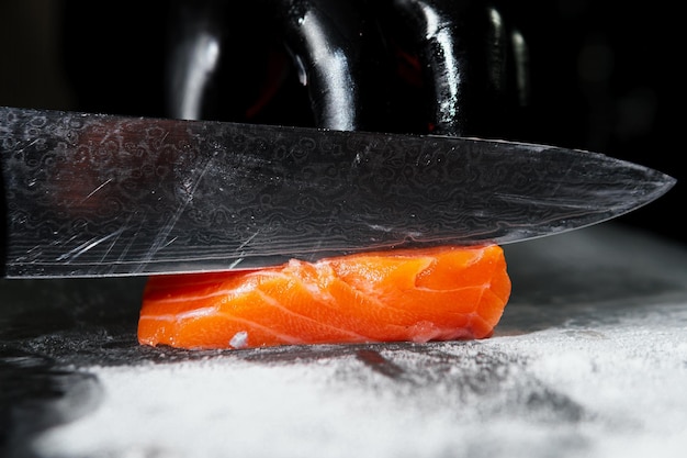 Nahaufnahme der Hand des Küchenchefs, die zum Kochen von frischem Lachsfilet auf schwarzem Hintergrund zubereitet wird