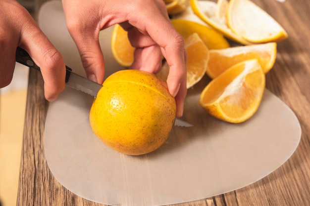 Nahaufnahme der Hand des lateinischen Mädchens 39, die eine orange Frucht in Scheiben schneidet