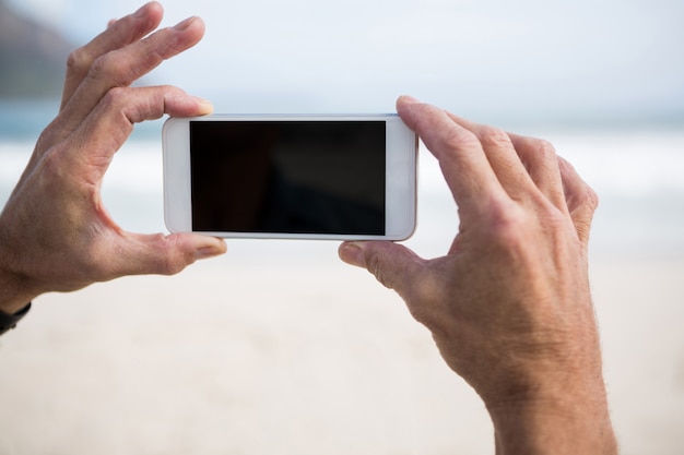 Nahaufnahme der Hand des Mannes, die Foto auf Handy am Strand macht