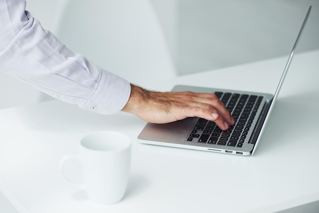 Nahaufnahme der Hand des Mannes, die im Büro auf dem Laptop tippt