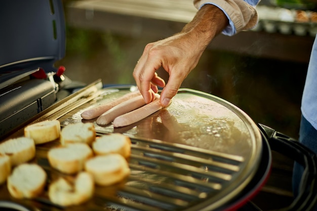 Nahaufnahme der Hand des Mannes, Würstchen und Bruschetta auf dem Grillgasgrill