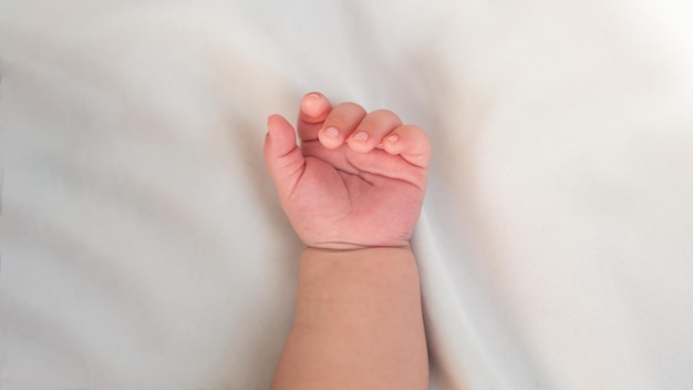 Nahaufnahme der Hand des neugeborenen Jungen auf weißem Blatthintergrund Baby schläft auf dem Bett