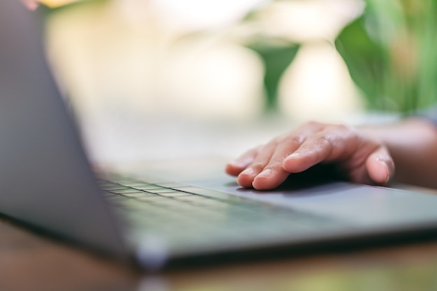 Nahaufnahme der Hand, die das Laptop-Touchpad auf einem Holztisch verwendet und berührt