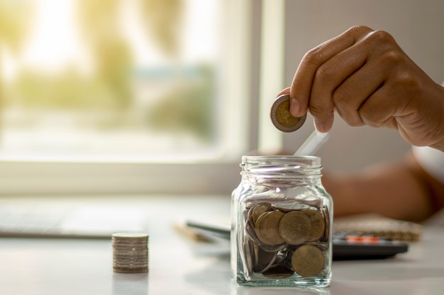 Nahaufnahme der Hand, die Münze in eine Flasche setzt, Geld spart, Geld sparendes Konzept für Finanzbuchhaltung.