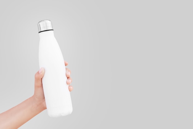 Nahaufnahme der Hand, die weiße wiederverwendbare Stahl-Thermowasserflasche hält, isoliert auf der ultimativen grauen Farbe, Trend 2021; mit Kopierplatz.