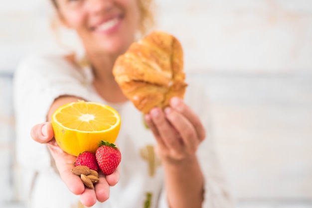 Nahaufnahme der Hand einer Frau, die eine Orange und eine Erdbeere hält und in der anderen Hand ein Croissant - Diät und gesunder Lebensstil und Konzept