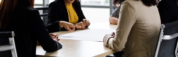 Nahaufnahme der Hand einer nicht identifizierten, nicht erkennbaren Geschäftsfrau, die auf leeres Papier auf dem Besprechungstisch im Konferenzraum zeigt, während andere über die Planung der Geschäftsstrategie als Teamarbeit im Unternehmen diskutieren.