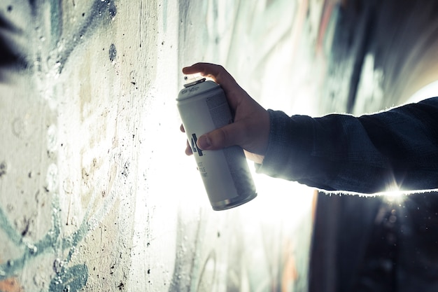 Nahaufnahme der Hand einer Person, die Graffiti mit Spraydose auf Wand malt