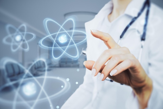 Nahaufnahme der Hand einer Ärztin, die auf ein abstraktes, leuchtendes Atomhologramm auf einem verschwommenen Krankenhaus- oder Klinikinnenhintergrund zeigt Nuklearmedizinisches Energie- und medizinisches Forschungskonzept