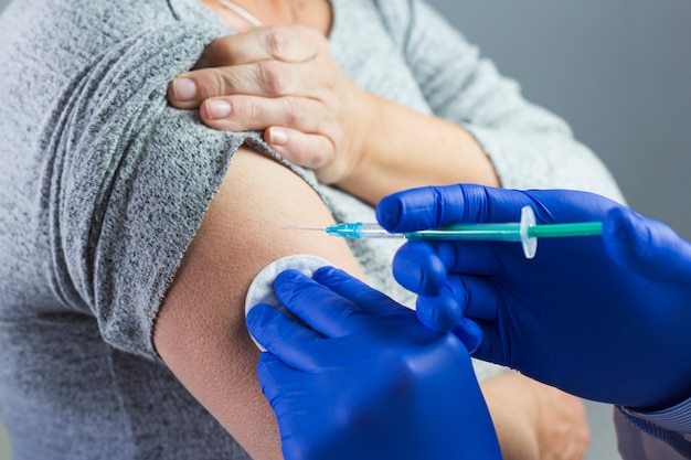 Nahaufnahme der Hand eines Doktors, welche die blauen Handschuhe geben Spritze auf dem Arm des Patienten trägt