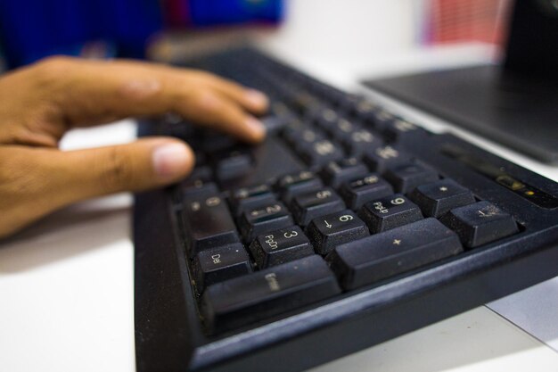 Nahaufnahme der Hand eines jungen Mannes, der zu Hause an einem Laptop mit digitalem Tablet auf dem Schreibtisch oder Kaffee arbeitet