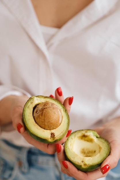 Nahaufnahme der Hand eines Mädchens, die eine Avocado hält, die in zwei Hälften geschnitten wird