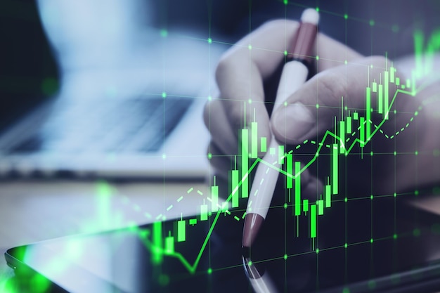 Nahaufnahme der Hand mit digitalem Tablett mit Stift und wachsendem grünen Candlestick-Diagramm auf verschwommenem Desktop-Hintergrund Devisenhandel und Finanzkonzept Doppelbelichtung