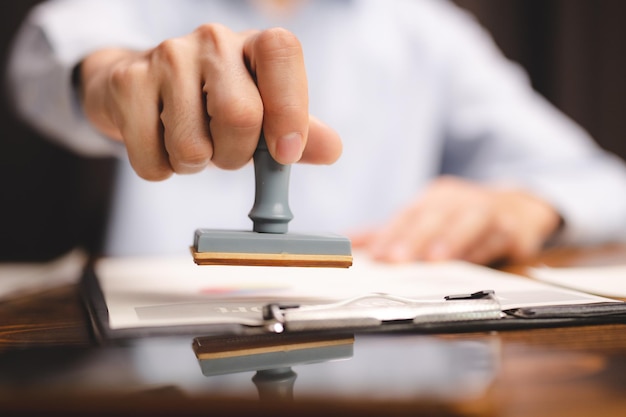 Nahaufnahme der Handstempelung einer Person mit bestandenem und genehmigtem Stempel auf dem öffentlichen Papier des Zertifikatsdokuments am Notar oder Geschäftsleute arbeiten von zu Hause aus isoliert für den Schutz vor Coronavirus COVID19