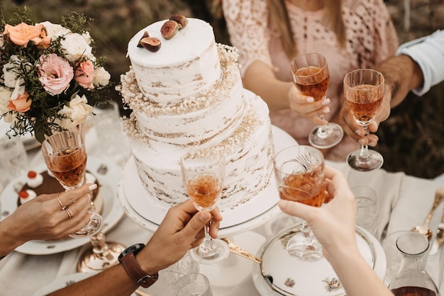 Nahaufnahme der Hochzeitstafel mit Kuchen und Menschen, die Gläser mit Getränken halten