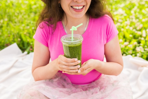 Nahaufnahme der jungen Frau haben Spaß im Park und trinken grüne Smoothies bei einem Picknick.