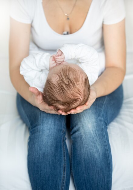 Nahaufnahme der jungen fürsorglichen Mutter, die den Kopf ihres kleinen Babys hält