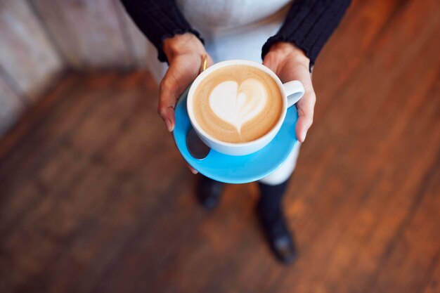 Nahaufnahme der Kellnerin im Café mit Tasse mit Herz-Design in Milch gegossen