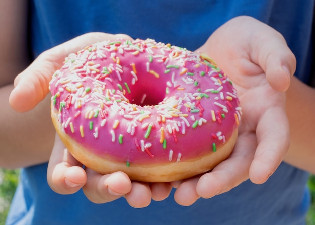 Nahaufnahme der Kinderhände, die einen Donut mit rosa Zuckerguss halten und streuen