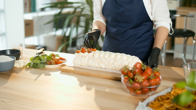 Nahaufnahme. Der Konditor legt frische Erdbeeren auf einen Baiserkuchen mit Sahne.